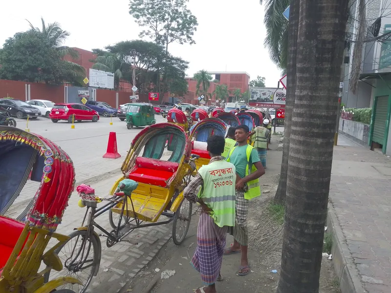 客待ちのリキシャが縁石沿いに並ぶ。ベストの番号は地区の住民団体の登録で、市内共通の制度ではない