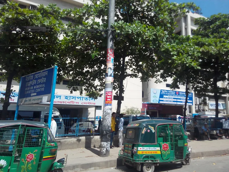 緑のCNG（三輪オート）。側面は金網で、車体には「সি.এন.জি চালিত」＝CNG動力の表示が入る