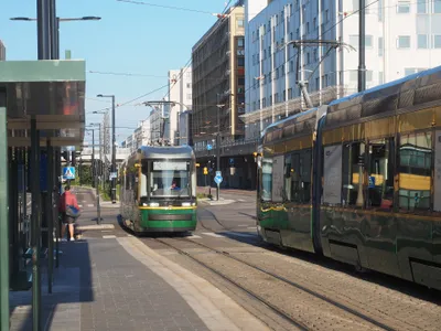 路上の停留所に入ってくるヘルシンキのトラム。緑と黄の車体で、前面に系統番号と行き先が出る