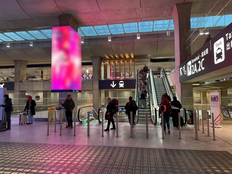 CDGターミナル2の駅コンコース。頭上の黒い案内は下向き矢印＋列車＝ホームへ、右手の「Taxis」表示がタクシー乗り場の方向