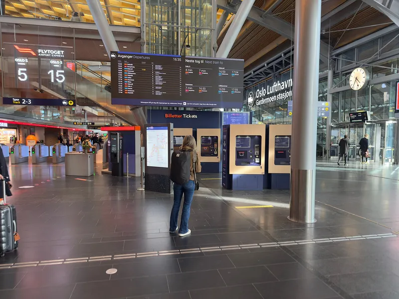 空港駅のコンコース。左がFlytogetのホーム（2・3番線）へ通じる改札で、券を買わなくてもここのリーダーにカードをかざせば通れる。中央の「Billetter Tickets」はVy・SJ・Go-Aheadの列車きっぷを売るEnturの券売機