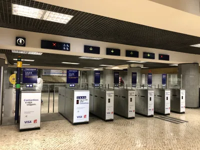 レスタウラドーレス駅の改札。ゲートに「Contactless e siga viagem／Tap to ride with contactless」の案内、その上のガラス仕切りには緑枠のステッカーで「財布ごとではなくカードをかざせ」とある
