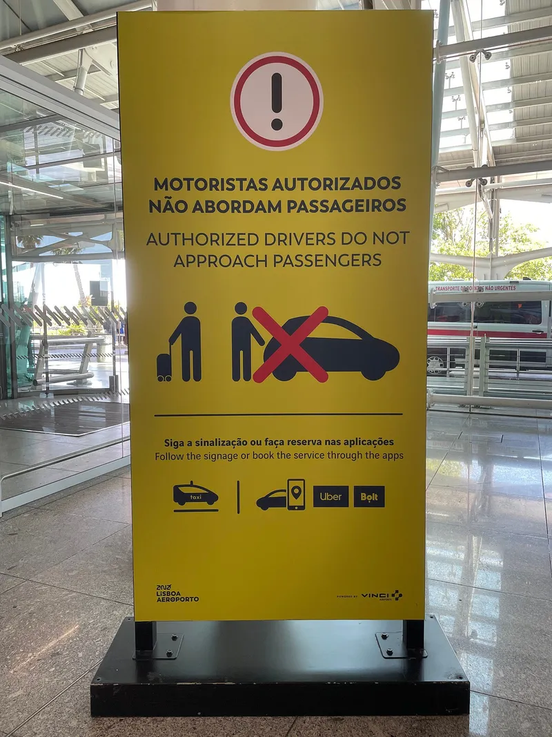 リスボン空港ターミナル1の掲示。「認可された運転手は乗客に声をかけない」「案内表示に従うか、アプリで予約を」とあり、タクシーとUber・Boltのロゴが並ぶ